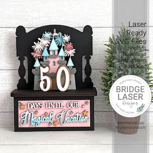 Könnte beinhalten: Ein lasergeschnittenes Holz-Countdown-Display mit einem rosa Schloss, blauen Türmen und der Zahl 50. Auf dem Display steht "DAYS UNTIL OUR Magical Vacation". Das Design umfasst Sterne und florale Akzente.