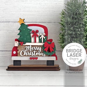 May include: A layered wooden cutout of a red truck bed carrying a green Christmas tree, two gift boxes with bows, and a wreath. The truck features a sign with the text Merry Christmas, three small red hearts, and a yellow star on the tree.