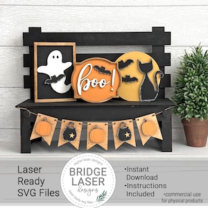 Könnte beinhalten: Eine schwarze Holzbank zeigt Halloween-Dekorationen. Ein gerahmter Geist, ein Schild mit "boo!" und Fledermäusen sowie eine Katzensilhouette vor einem gelben Mond sind zu sehen. Ein Banner mit Kürbissen und Kesseln hängt darunter. Der Text "Laser Ready SVG Files".