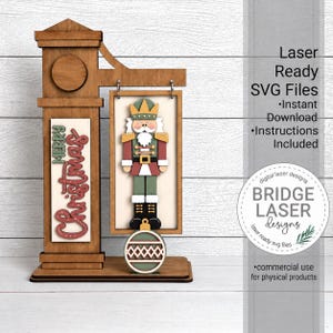 May include: A wooden laser-cut sign featuring a nutcracker figure hanging from a post, with the text Merry Christmas in red and green. A round ornament hangs below the nutcracker. The image includes text: Laser Ready SVG Files, Instant Download, Instructions Included, and Bridge Laser Designs.