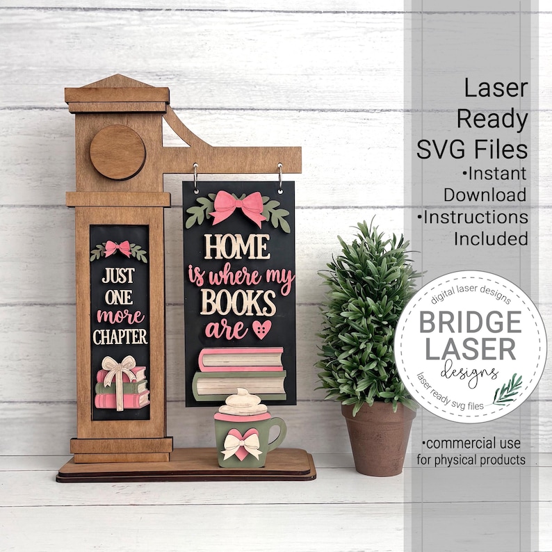 May include: A wooden laser-cut sign featuring a vertical post and a hanging rectangular plaque. The text reads "JUST ONE more CHAPTER" and "HOME is where my BOOKS are" with decorative book, bow, and mug cutouts in pink, green, and tan colors.