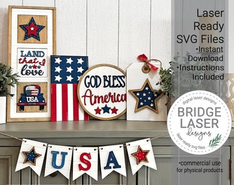 May include: A set of five laser cut wood signs with a patriotic theme. The signs feature stars, stripes, and the words "Land that I love", "USA", "God Bless America", and "USA".