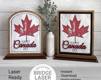 May include: Two wooden Canada Day signs. Each sign features a red maple leaf design on a white background, with the words "Happy Canada Day" in red script. One sign has an arched top, the other is rectangular.