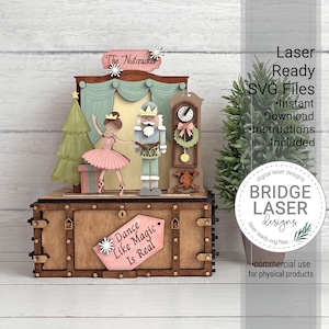 K&ouml;nnte beinhalten: Ein lasergeschnittenes Holzdisplay zum Thema Nussknacker mit einer Ballerina, einem Nussknacker-Soldaten, einer Standuhr und einem Weihnachtsbaum. Die Basis ist eine Holzkiste mit einem Schild, auf dem Dance Like Magic Is Real steht, und einem Schild The Nutcracker.