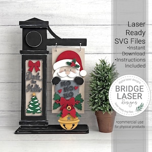 May include: A black wooden sign stand featuring a hanging rectangular plaque with a layered Santa Claus design, the text HO HO HO, a red bow, and a yellow bell. The stand includes a vertical panel with a red bow, the text Deck the Halls, and a tree.
