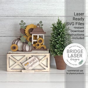 Op de afbeelding: Een gelaagde houten decoratieset met pompoenen, zonnebloemen, een lantaarn en een bordje met de tekst GATHER Together en twee kleine hartjes. Daarnaast staat een kleine groene plant in een pot. Tekst rechts: Laser Ready SVG Files.