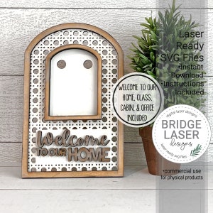 May include: A laser-cut wooden sign with a welcome to our home message. The sign has a woven pattern and a cutout window. The sign is on a wooden surface with a potted plant in the background. The text "Laser Ready SVG Files" is visible in the upper right corner of the image.