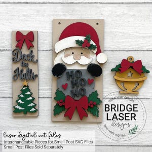 May include: A set of three wooden laser-cut Christmas decorations including a vertical sign with the text Deck the Halls, a Santa Claus figure holding a sign with the text HO HO HO, and a gold bell ornament, all featuring red bows and green holly.