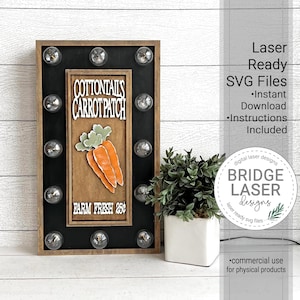 May include: A wooden sign with a black background and a brown frame. The sign has a white inscription that reads "COTTONTAIL'S CARROT PATCH FARM FRESH 250". The sign is decorated with a cartoon image of carrots and has eight light bulbs around the perimeter.