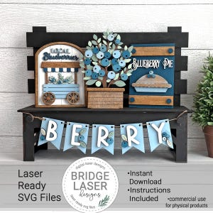 May include: A wooden decorative bench with blueberry-themed cutouts. Features a cart labeled "Local Blueberries", a blueberry tree, and a sign for "Blueberry Pie". A banner spells "BERRY". The design includes the text "Laser Ready SVG Files".