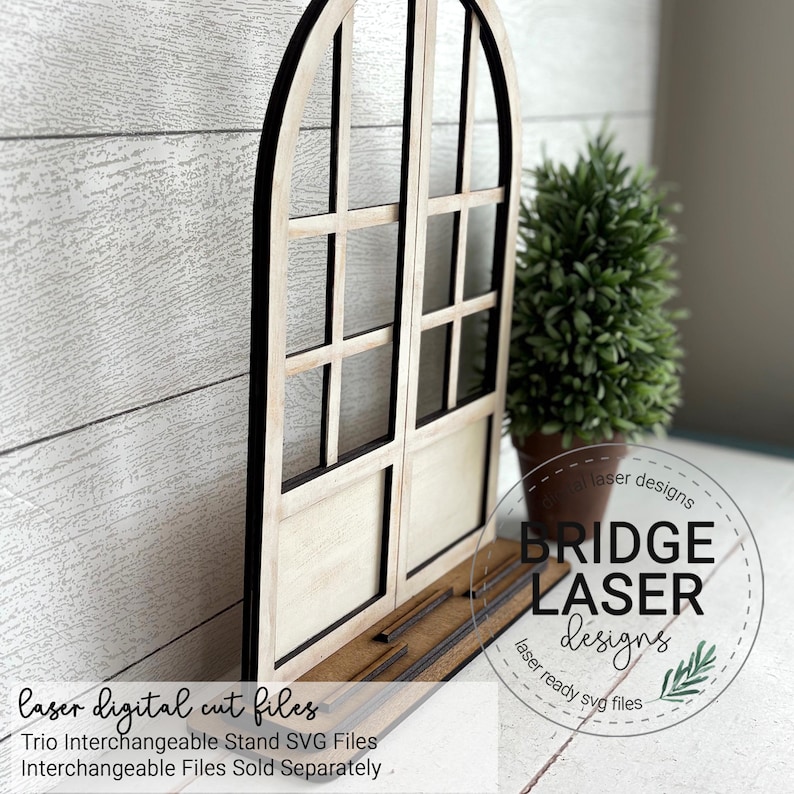 May include: A wooden arched window frame with a black border and cream-colored panels. The frame has a rectangular base with slots for interchangeable elements. The text "laser digital cut files" and "Bridge Laser Designs" are visible.