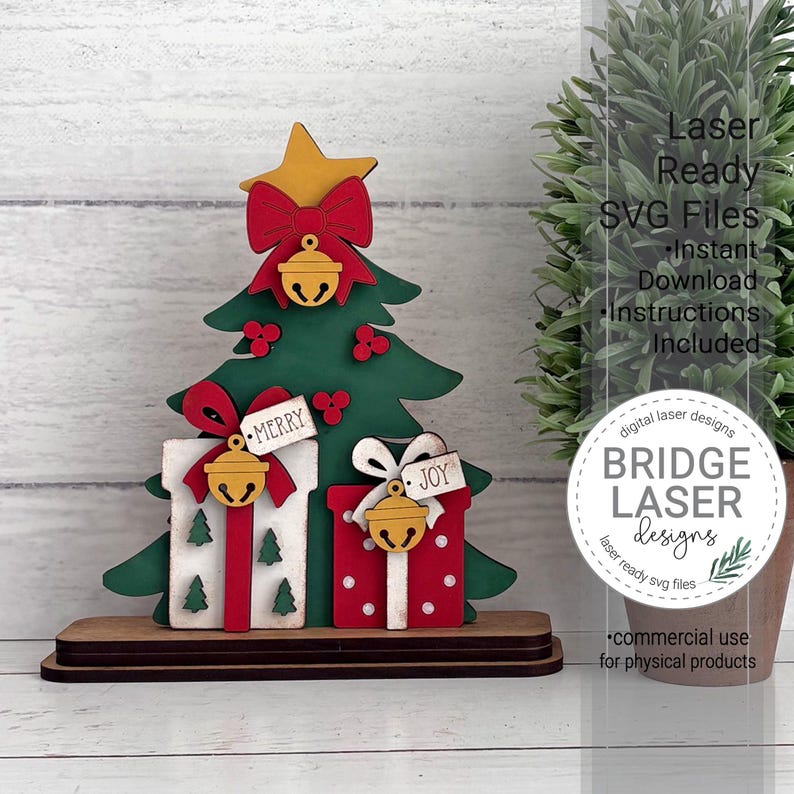 May include: A layered wooden Christmas tree decoration featuring a yellow star, red bows, and gold bells. Two gift boxes are at the base, one white with green trees and one red with white dots. Tags read Merry and Joy. Text includes Laser Ready SVG Files.