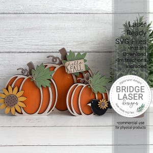 May include: Three layered wooden pumpkin cutouts in orange with green leaves, a yellow sunflower, and a black bird accent. A small rectangular sign attached to the center pumpkin reads "hello FALL". The text "Laser Ready SVG Files" is visible.