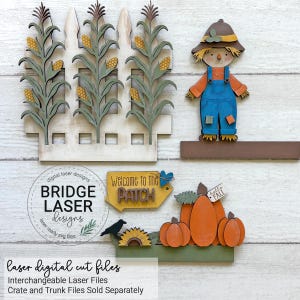 May include: A set of laser-cut wooden decorations featuring a white picket fence with corn stalks, a scarecrow in blue overalls, a yellow sign reading Welcome to the PATCH, a black crow, a sunflower, and orange pumpkins with a hello FALL tag.