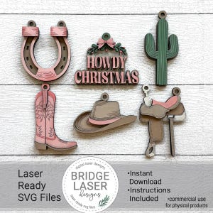 May include: A selection of laser-cut wooden Christmas decorations with a Western theme. The ornaments feature a horseshoe, cowboy boot, cowboy hat, cactus, and a saddle. The text "HOWDY CHRISTMAS" is included. The decorations are in shades of pink, brown, and green.