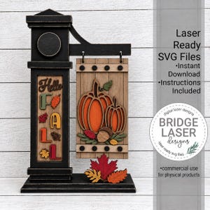 May include: A black wooden sign post with a hanging rectangular panel featuring layered orange pumpkins, an acorn, and autumn leaves. The post displays the text Hello FALL with colorful leaf accents. Text on the right reads Laser Ready SVG Files.