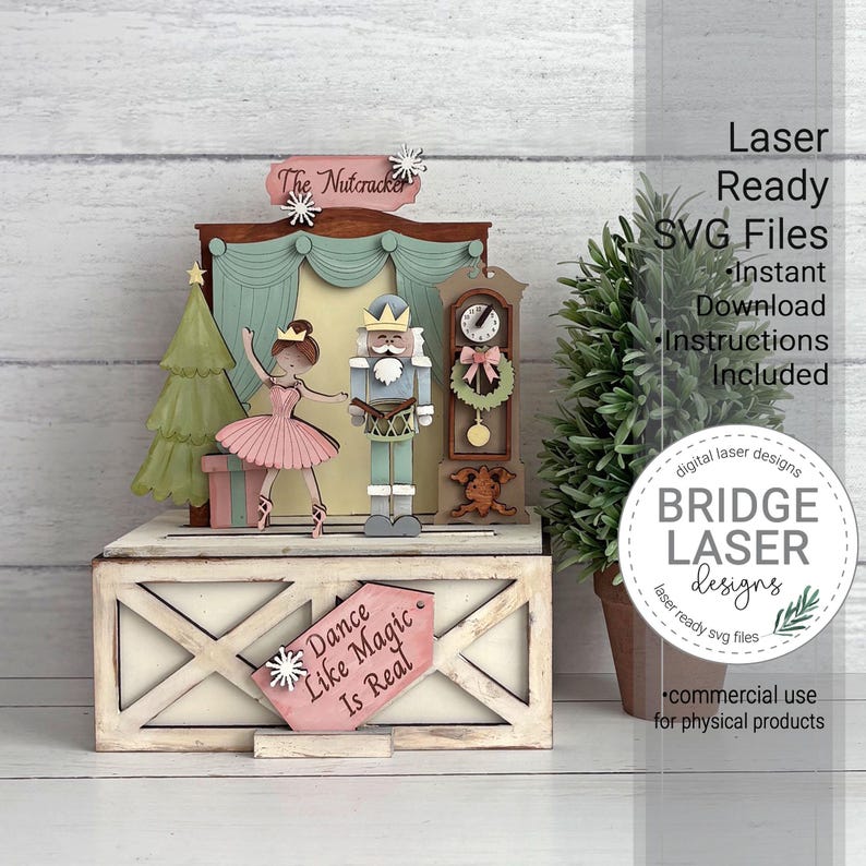 K&ouml;nnte beinhalten: Ein mehrschichtiges Holzdisplay mit einer Ballerina und einem Nussknacker auf einer B&uuml;hne, erg&auml;nzt durch einen Weihnachtsbaum und eine Standuhr. Die Basis tr&auml;gt das Schild "Dance Like Magic Is Real" und oben steht "The Nutcracker".