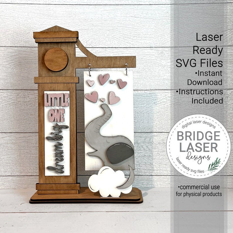 May include: A wooden sign with a pink elephant, hearts, and the words "Little One Dream Big". The sign is designed for laser cutting and comes with instructions.