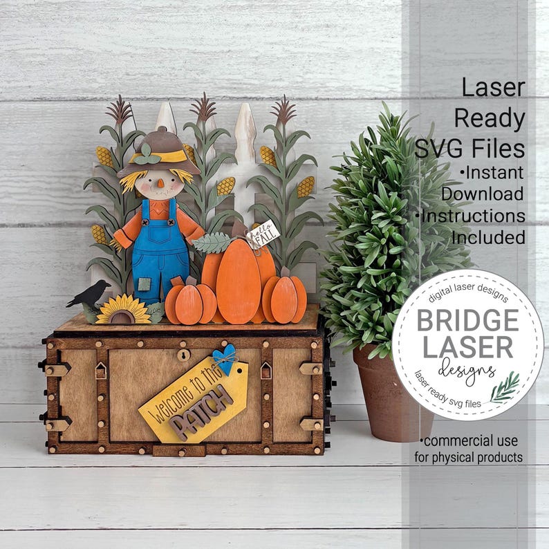 May include: A wooden laser-cut display featuring a scarecrow in blue overalls, orange pumpkins, and corn stalks standing on a rectangular box. A yellow tag attached to the front of the box reads Welcome to the PATCH with a small blue heart icon.