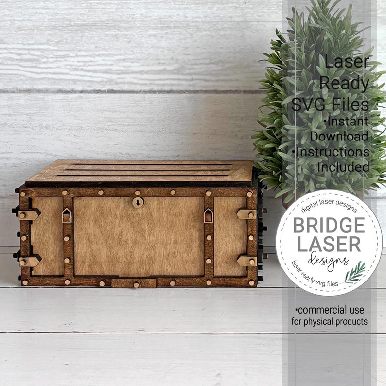 May include: A rectangular wooden box with a dark brown frame and a lighter brown centre panel, featuring decorative metal-like studs, corner brackets, and a central keyhole. The box has a slatted top and is positioned next to a small green plant.