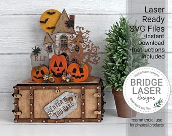 May include: A wooden Halloween-themed display box featuring a laser-cut haunted house, a yellow moon with black bats, three orange jack-o'-lanterns, a tombstone with the text R.I.P., and a sign that reads ENTER IF YOU DARE with small flowers.