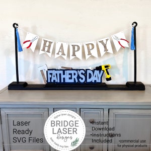 May include: A Father's Day banner with the words "HAPPY FATHER'S DAY" in a decorative design. The banner includes tools and blue tassels. The design is displayed on a black base.