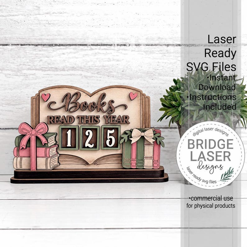 May include: A laser-cut wooden sign featuring the text Books READ THIS YEAR with the number 125 displayed in three square frames. The design includes stacks of books decorated with pink and green bows and small pink hearts on a dark base.