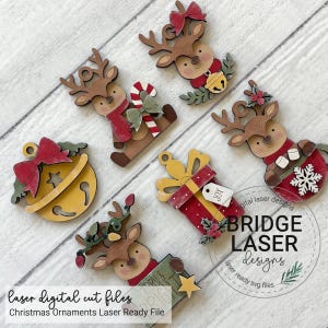 May include: A collection of six wooden Christmas ornaments featuring reindeer, a jingle bell, and a gift box. The reindeer designs include accessories like a candy cane, a snowflake, and string lights. Each ornament has a hole for hanging.