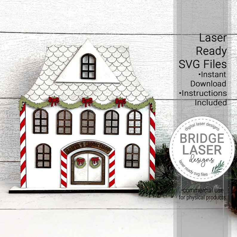 May include: A white wooden Santa's Workshop building with red and white candy cane trim, green garland, and red bows. The building has a sign that reads "Santa's Workshop".