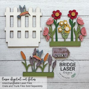 K&ouml;nnte beinhalten: Ein Set aus lasergeschnittenen Holzteilen, bestehend aus einem wei&szlig;en Lattenzaun mit Kolibri, einer gr&uuml;nen Basis mit roten und gelben Blumen, einer gr&uuml;nen Basis mit violetten Pflanzen und einem Kolibri sowie einem Schild mit der Aufschrift The Hummingbird GARDEN.