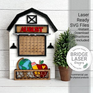 May include: A wooden farmhouse-style calendar with a black roof and white siding. The calendar features a red August sign and a black and white calendar grid for the month of August. The calendar is decorated with a globe, pencil, and apple. The calendar is laser cut and ready to assemble.