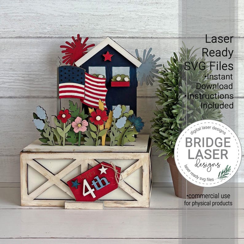 May include: A layered wooden craft display featuring a dark blue house with an American flag, red and blue fireworks, and colorful flowers. The base is a white farmhouse-style box with a red tag labeled 4th, accompanied by a small green potted tree.