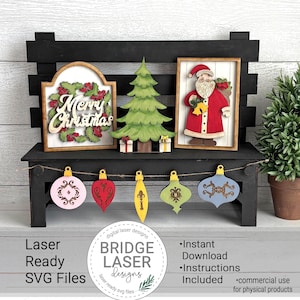May include: A black wooden bench displays Christmas-themed decorations. These include a sign with "Merry Christmas", a green tree, and a Santa Claus figure. Below, a garland holds various ornaments. The image also includes the text "Laser Ready SVG Files".
