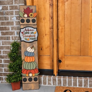 May include: A tall, rectangular wooden porch sign featuring a stack of five pumpkins in white, blue, orange, green, and red. The sign includes a central plaque with the text Autumn Leaves and Pumpkins Please, topped with a maple leaf and sunflower.