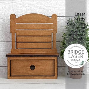 May include: A wooden decorative shelf with a drawer and a back with horizontal slats. The shelf is made of light brown wood and has a small drawer with a circular handle. The image includes text that says "Laser Ready SVG Files" and "BRIDGE LASER designs".