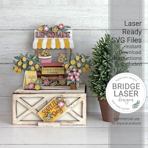 May include: A multi-layered wooden lemonade stand display featuring a yellow and white striped awning, lemon trees, pink flowers, and a sign that reads Squeeze the Day. The structure includes text reading Lemonade and Farm Fresh Lemons.