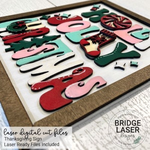 May include: A square wooden sign featuring layered, multi-colored cutouts spelling out Jolly Christmas. The design includes red, pink, white, and dark green elements, such as a peppermint candy, a stocking, and pine trees, all set within a dark wood frame.