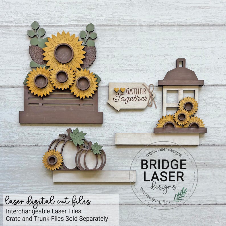 Op de afbeelding: Een set lasergesneden houten knutselstukken met zonnebloemen in een bruine krat, twee pompoenen met groene bladeren, een lantaarn met zonnebloemen en een bordje met twee kleine hartjes en de tekst Gather Together. Inclusief het Bridge Laser Designs logo.