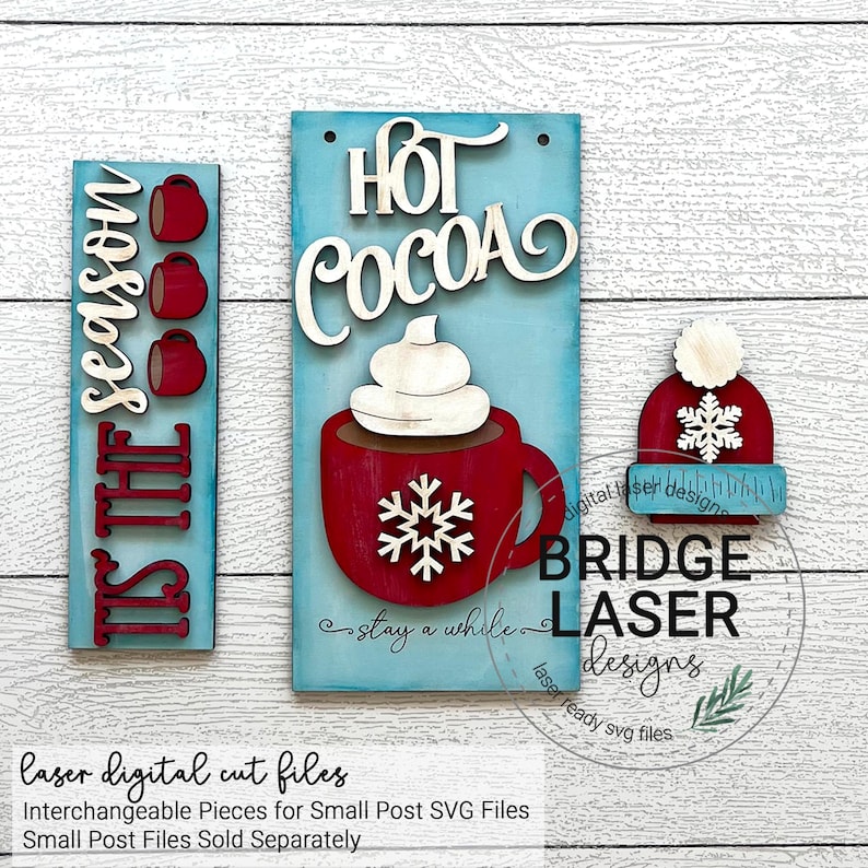 K&ouml;nnte beinhalten: Ein Set aus drei lasergeschnittenen Holzschildern mit Winterthema. Die Schilder zeigen den Text "Tis the season", "Hot Cocoa" und ein Schneeflocke. Die Schilder sind in Rot, Wei&szlig; und Blau bemalt.