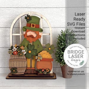 May include: A wooden St. Patrick's Day decoration featuring a leprechaun figure with a green hat and coat, standing in front of a window. A barrel of flowers and a pot of gold are on either side. The text "Laser Ready SVG Files" is visible.