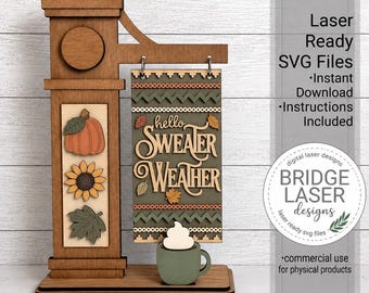 May include: A wooden laser-cut display stand featuring a hanging sign that reads hello SWEATER WEATHER. The sign is decorated with autumn leaves and geometric patterns. A small mug with a white foam top sits at the base, and a vertical panel displays a pumpkin, a sunflower, and a leaf.