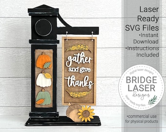 May include: A wooden sign with the text "gather and give thanks" and a black metal stand with pumpkins and leaves. The sign is for a laser cutting project.