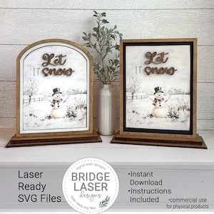 May include: Two wooden framed signs with a winter scene featuring a snowman and the words "Let It Snow." The signs have a brown base and frame, with a white background. One sign is arched, the other rectangular.