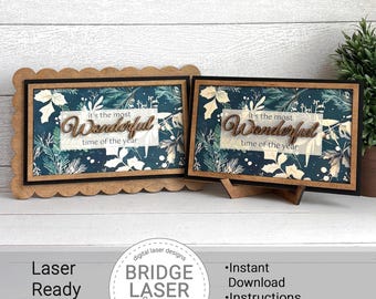 May include: Two wooden framed art pieces with the text "it's the most Wonderful time of the year". The art features a dark teal background with white and green floral accents. One frame has a scalloped edge, the other has a stand.