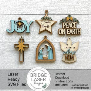 May include: A collection of laser-cut wooden Christmas ornaments. The ornaments include the words "JOY", "PEACE ON EARTH", and "adore HIM". Other ornaments include a star, a cross, an angel, and a nativity scene. The ornaments are in various colors.