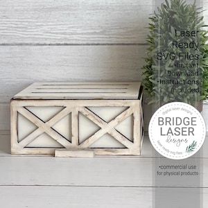 May include: A rectangular wooden box with a distressed white finish and a cross-brace design on the front panel. The top features horizontal slats. A circular logo on the right reads: digital laser designs BRIDGE LASER designs.