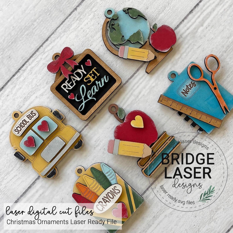 May include: A set of six school-themed wooden ornaments featuring a globe with a pencil and apple, a chalkboard with the text READY SET LEARN, a blue notebook with scissors and a ruler, a yellow school bus, an apple with a pencil, and a box of crayons.