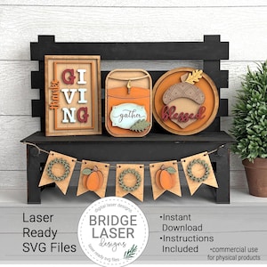 Könnte beinhalten: Eine herbstliche Holzdekoration mit einem Banner mit Kürbissen und Kränzen sowie drei dekorativen Schildern mit den Aufschriften "Giving", "Gather" und "Blessed". Die Dekoration steht auf einer schwarzen Bank. Laserfertige SVG-Dateien.