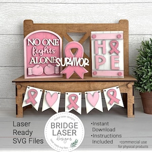 Peut inclure: Ensemble d&eacute;coratif en bois avec des accents roses, comprenant une banni&egrave;re, des panneaux avec les mots "NO ONE fights ALONE" et "HOPE", et un ruban rose. L'ensemble est con&ccedil;u pour la d&eacute;coupe laser et comprend des fichiers SVG.
