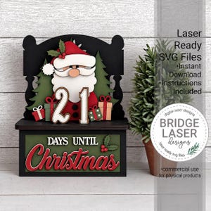 May include: A layered wooden Christmas countdown sign featuring a Santa Claus figure, green pine trees, and gift boxes. The sign displays the number 21 and the text DAYS UNTIL Christmas in red and white lettering on a black and green base.